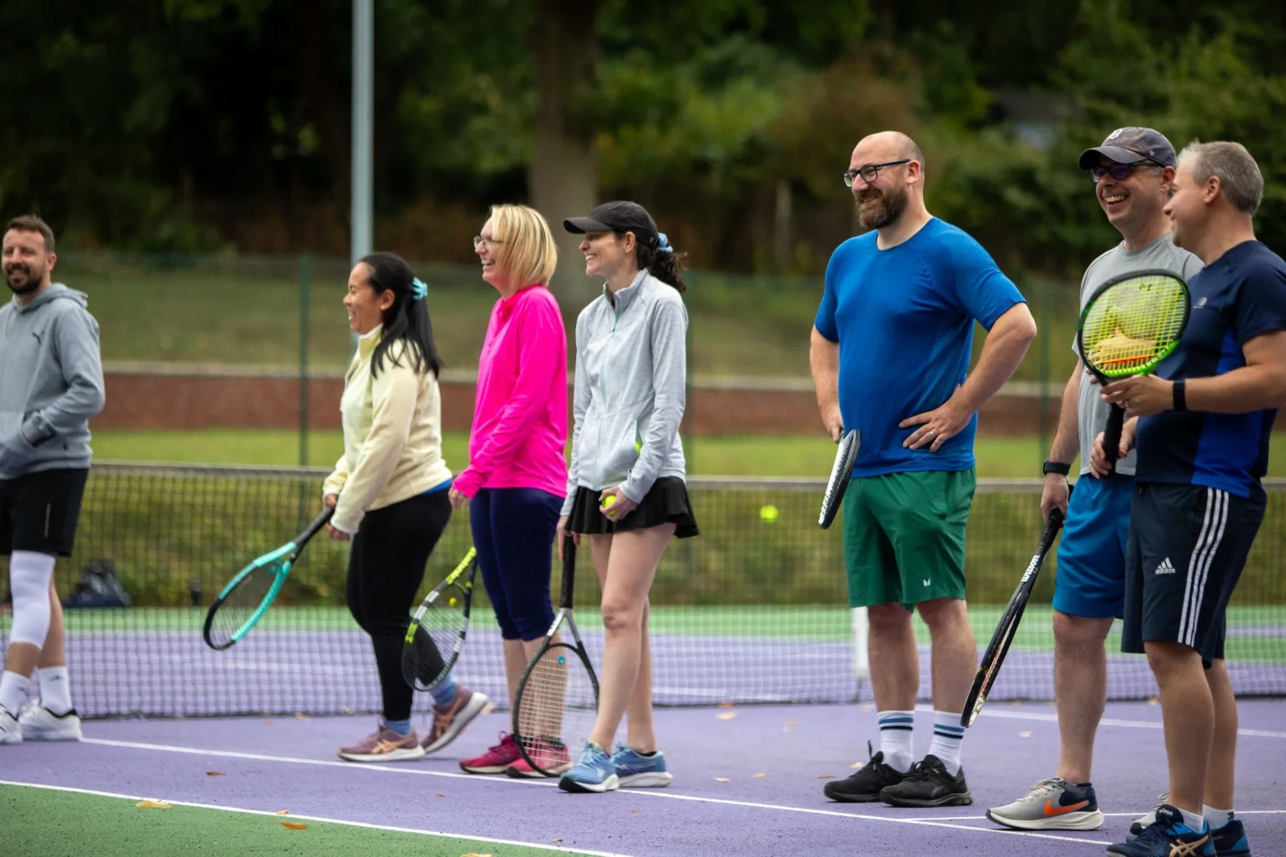 A friendly group of adult tennis players standing together on court with rackets
