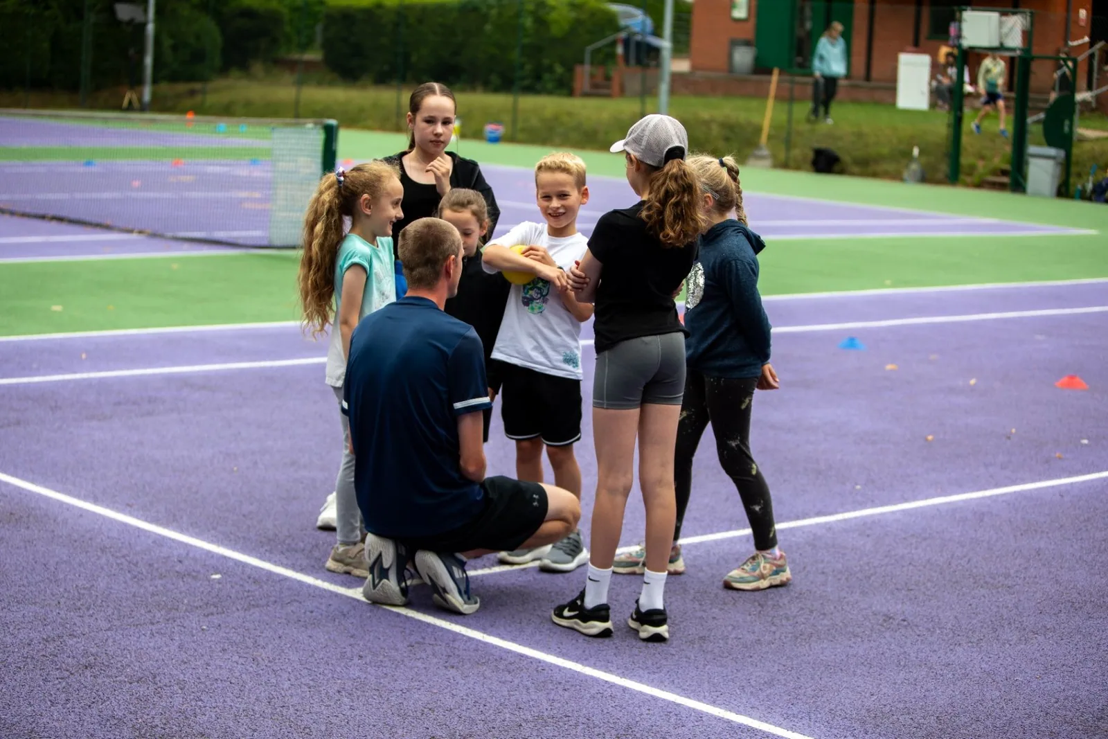 MH Tennis coach gathering with young players on a colourful outdoor court