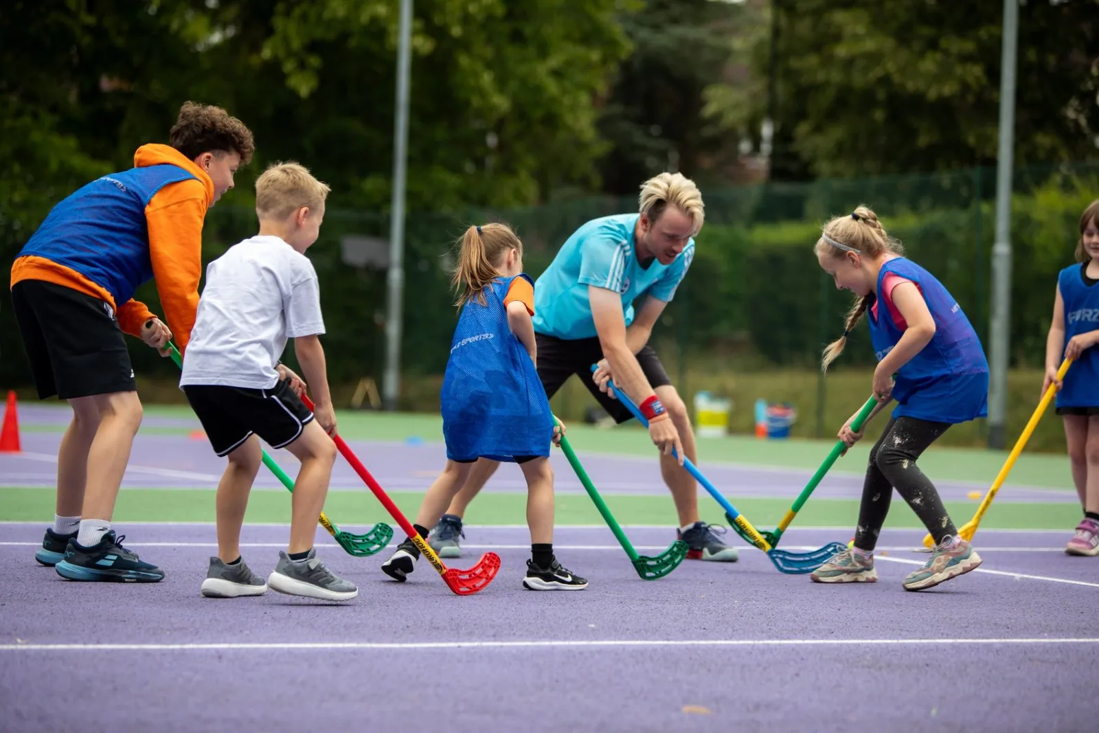 Young players taking part in a hockey activity with sticks on a tennis court