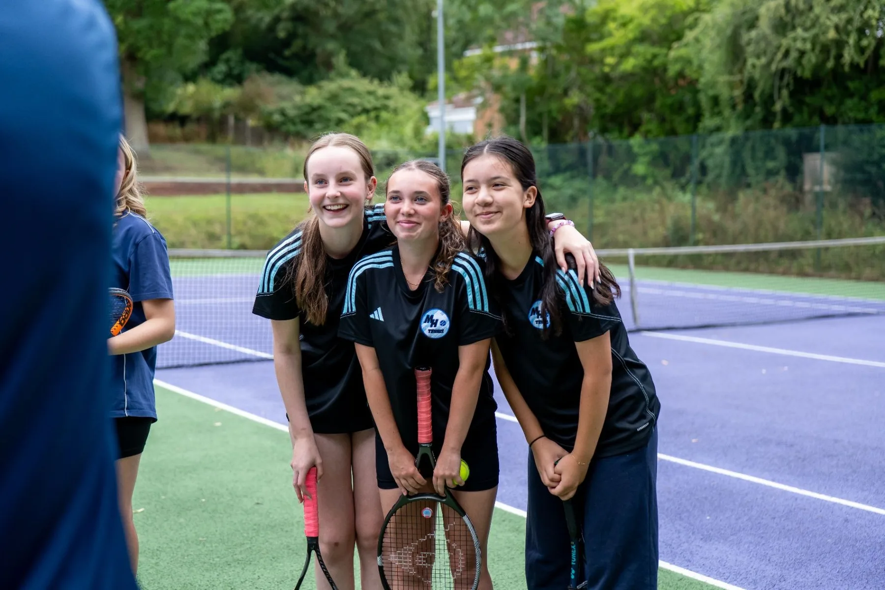 Three smiling young tennis leaders standing together on an outdoor court