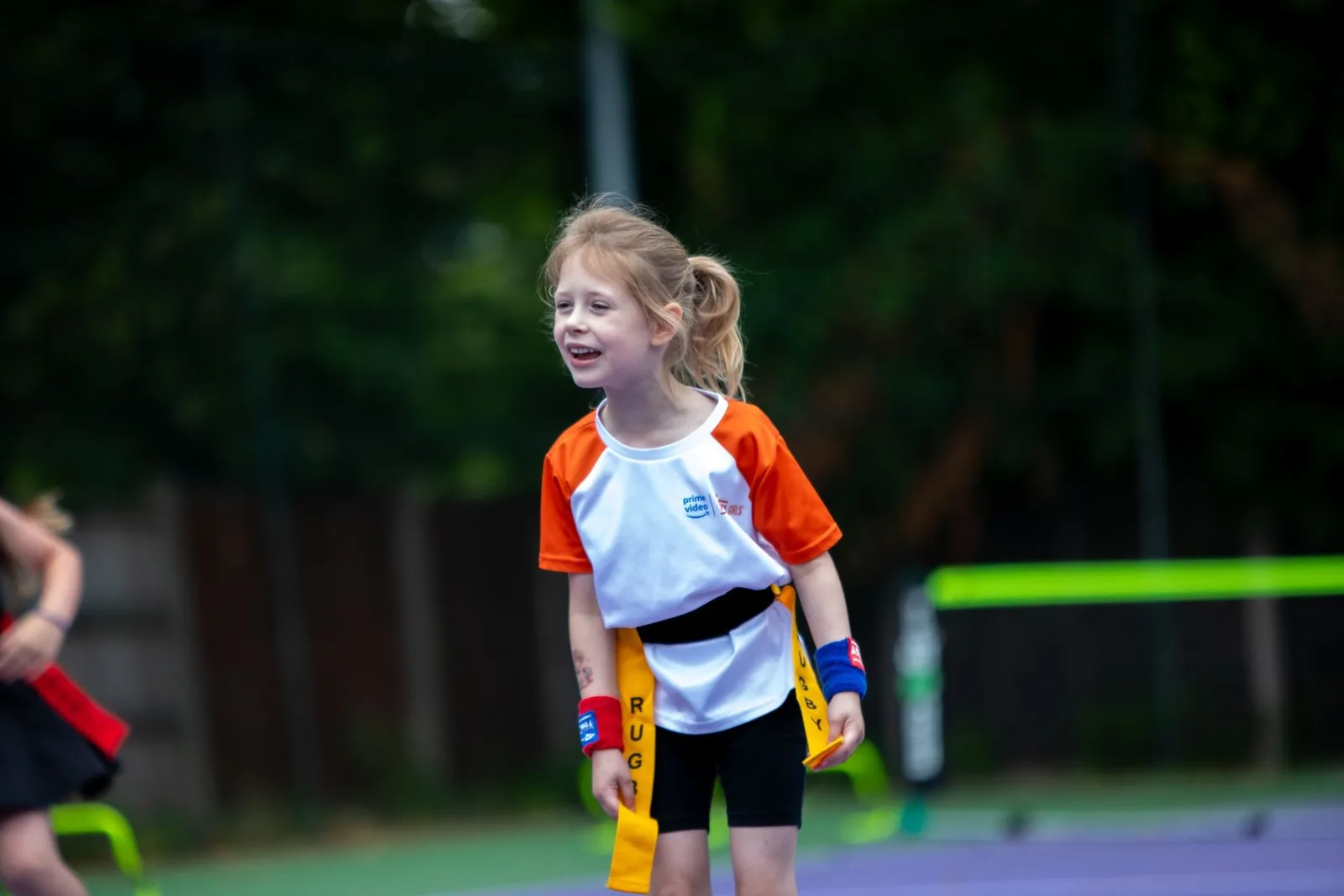 Young girl smiling on an outdoor tennis court with a racket
