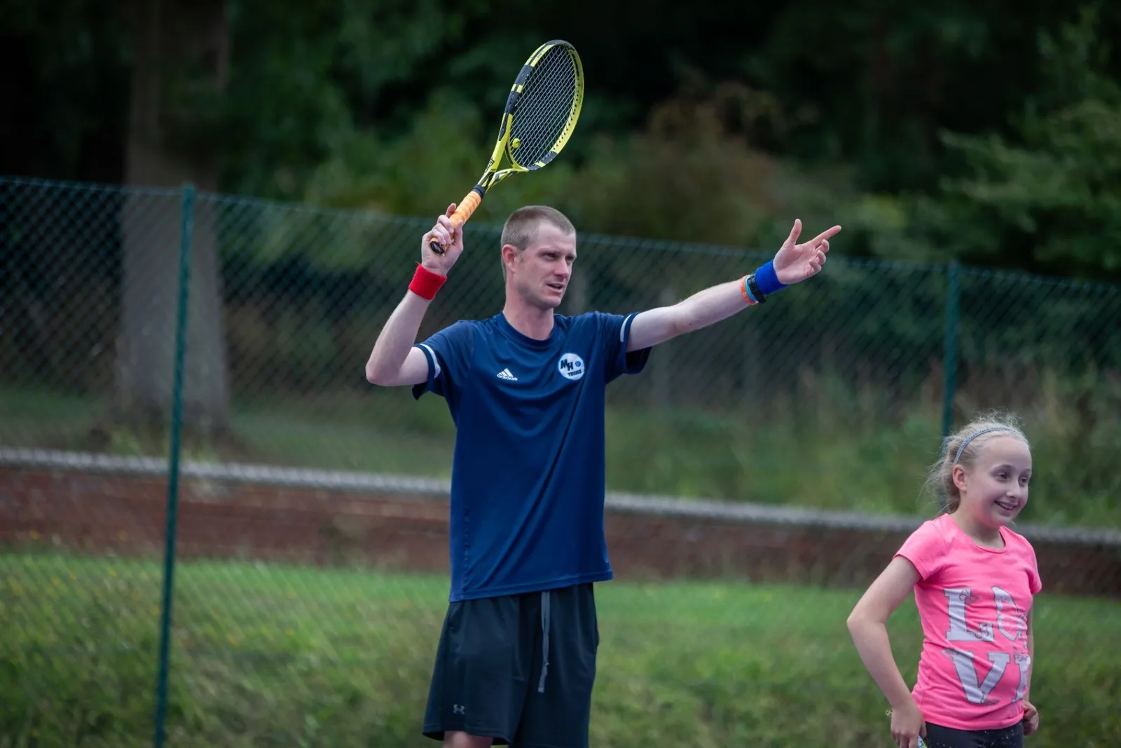 Coach demonstrating a tennis stroke beside a young player