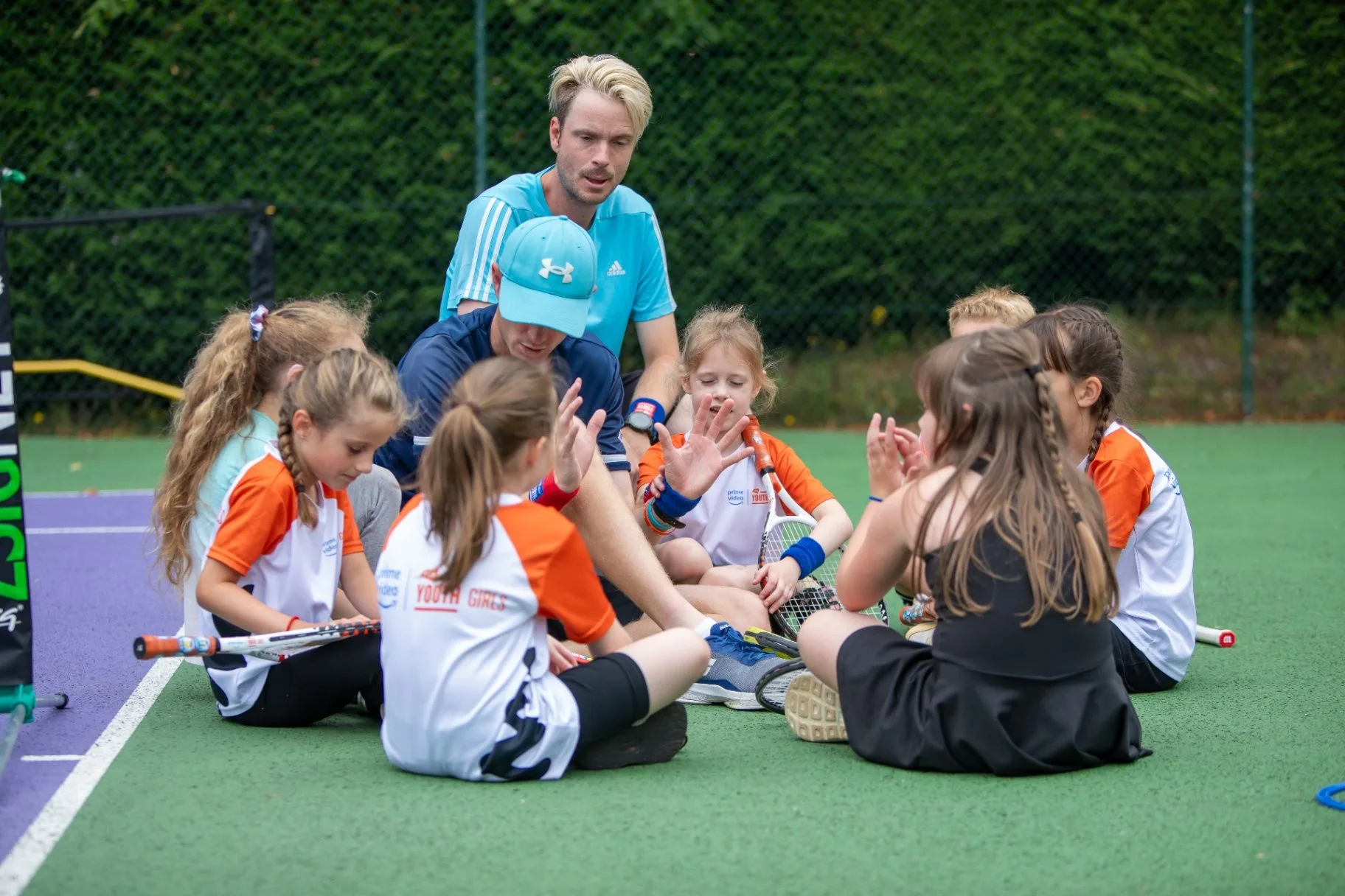 Tennis coach talking with a group of girls seated on an outdoor court