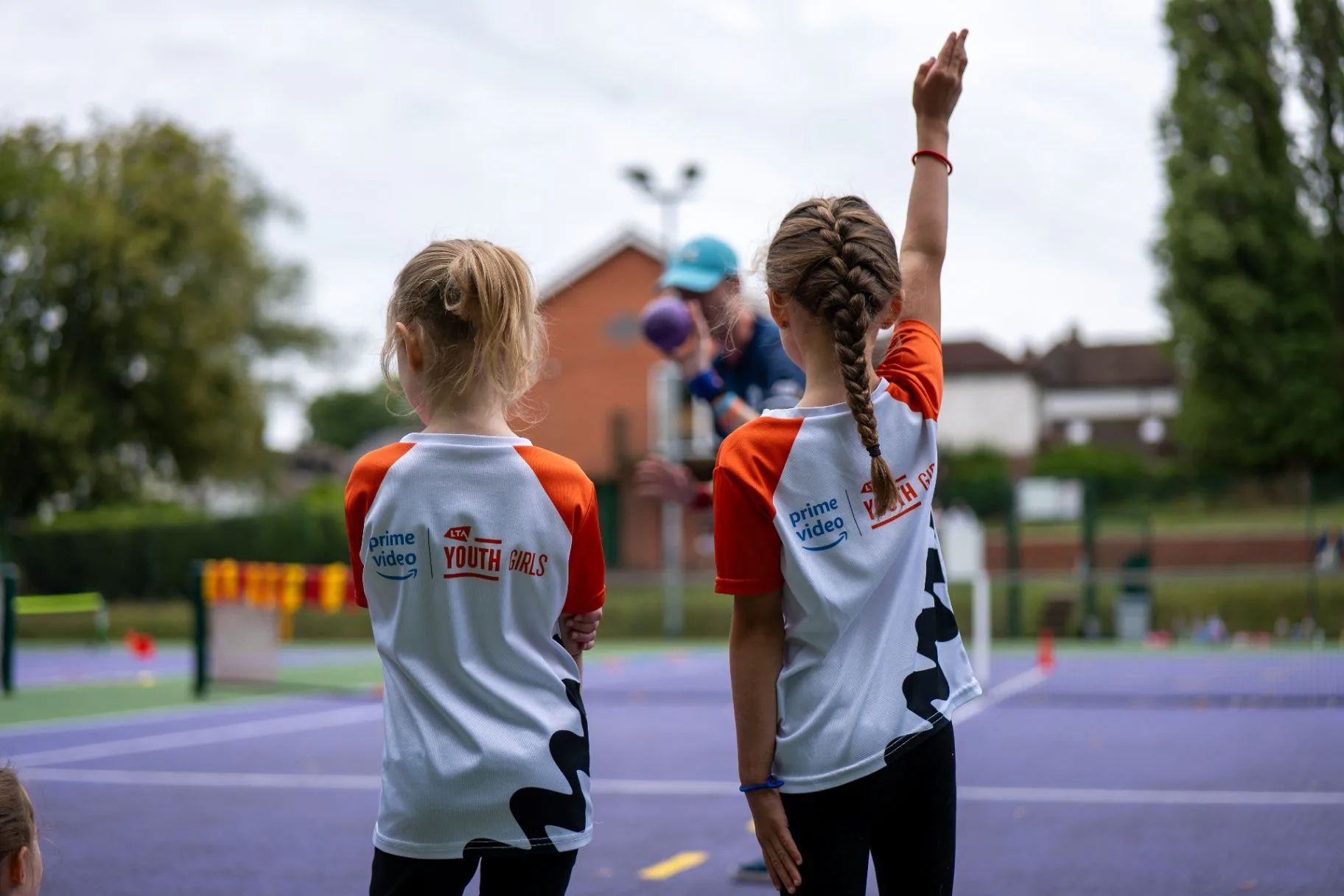 Two girls raising their hands during an outdoor tennis activity